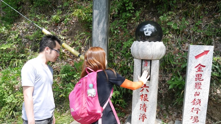 1号路の途中には、「六根清浄」（ろっこんしょうじょう）と書かれた石碑があります。六根とは、人間が備える認識の根幹のこと。みおが手を添えた部分を回すことで、石碑に書かれた六根を執着から解き放ち、清らかにすることができるそうです。