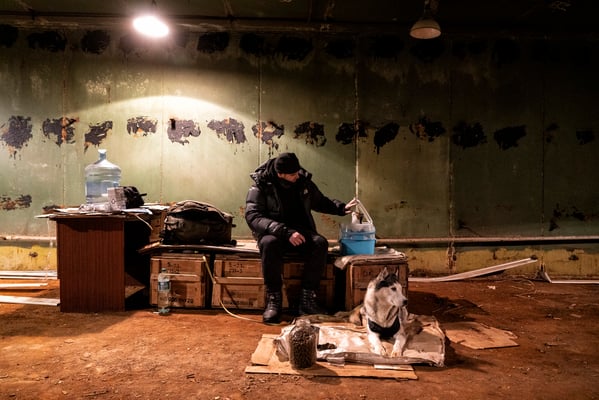 Timothy waiting for the air raid warning to end inside the bunker with his dog and cat.  This huge bunker room at the time contained the computers, now dismantled. Timothy sits on wood boxes containing the gas masks of the time.