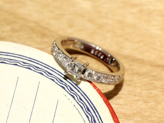 センターはスクエア（レクタンギュラーステップ）カットのダイヤモンド。アームにはラウンドカットのダイヤモンドを敷き詰めて。