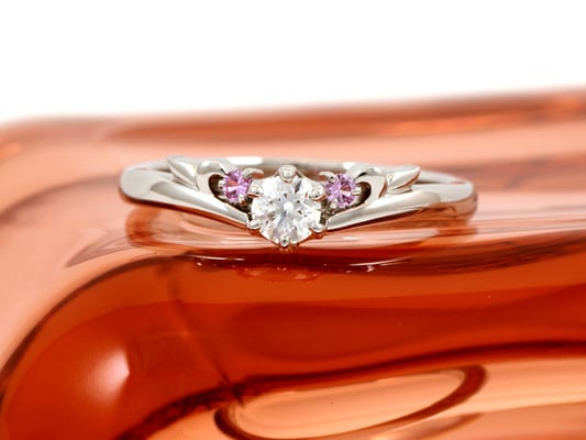 緩やかなV字ラインのエンゲージリング。サイドにピンクサファイアを添えて。