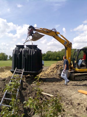 Die Wirbelbett- Kleinkläranlage aus Plastik  hängt an der Traverse des 7,50 t Minibaggers.