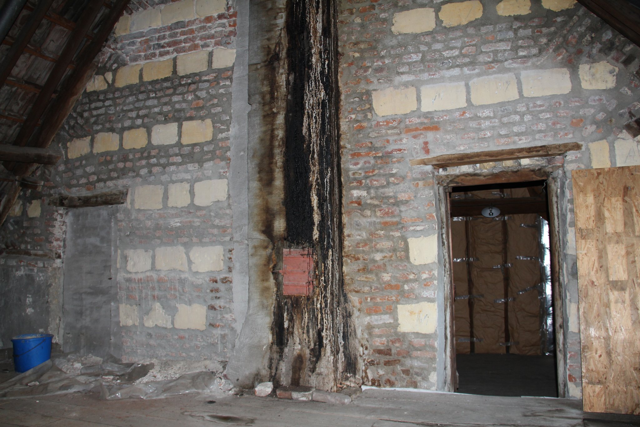 Brandmuur tussen voor- en achterhuis met mergelstenen speklagen en voormalige vensteropeningen voorhuis.