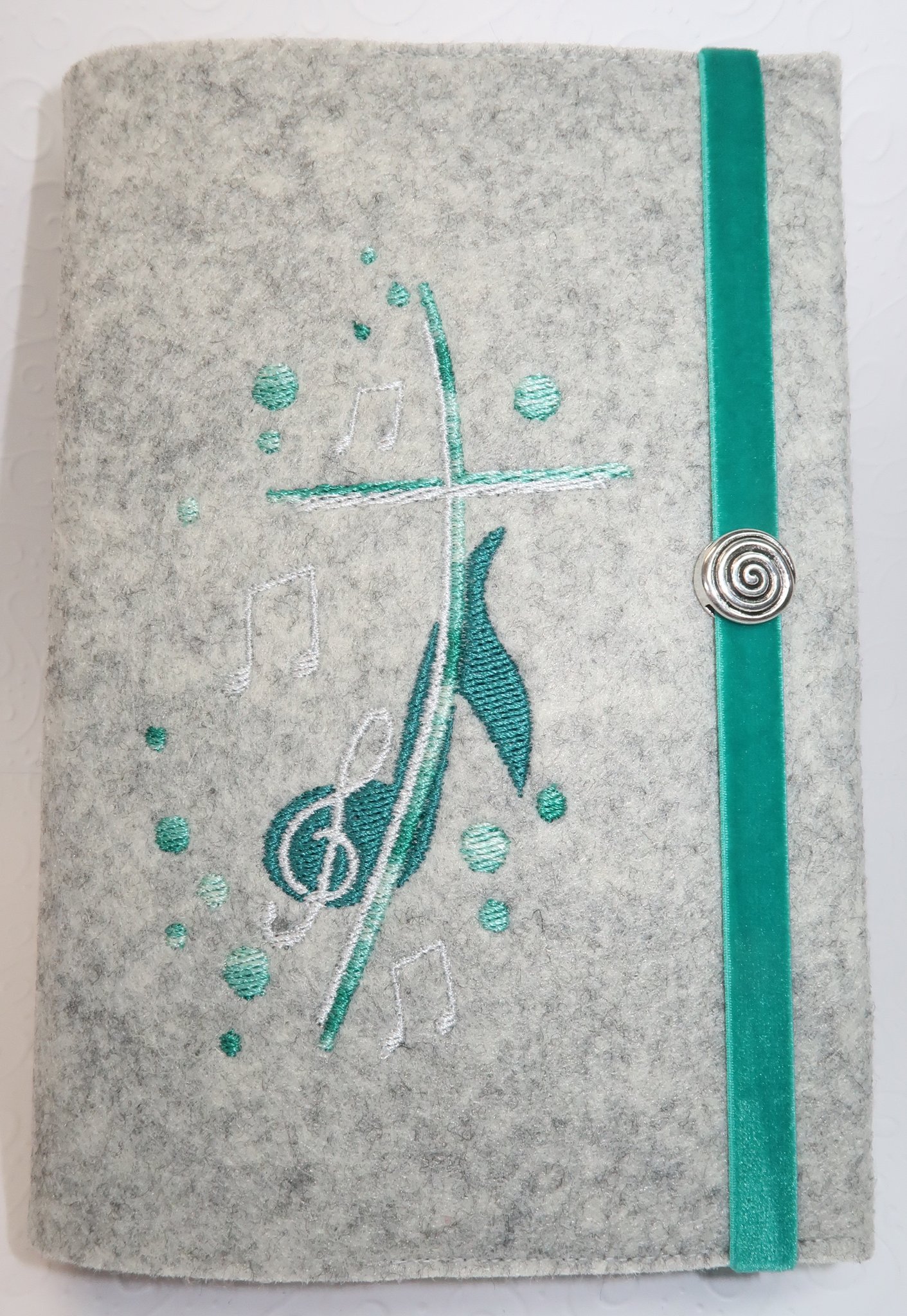 Einband ("Du bist ein Ton in Gottes Melodie" Basic) in Filz lichtgrau (neue Farbe!) mit Stickmotiv "Musik" in eukalyptus-mint-silber, Gummi mit samtiger Oberfläche, optional mit Metallspirale am Gummi