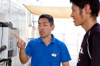 トマトのビニルハウス(下)の灌水(かんすり:水やり)システムの操作パネル / より高度な植物工場へ発展させる試みに取り組んでいる。右は、このシステムの開発管理をしている伊原さん。