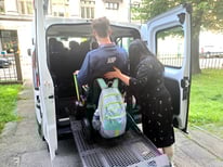 Young man in a wheelchair being assisted by a woman up a ramp int a white van