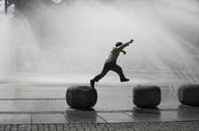 Junge springt über Steine an einem Springbrunnen