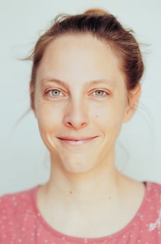 Ein Portrait von Anna Breuer, CranioSacral Therapeutin. Sie trägt ein rosa Shirt vor einem grauen Hintergrund und lächelt leicht.