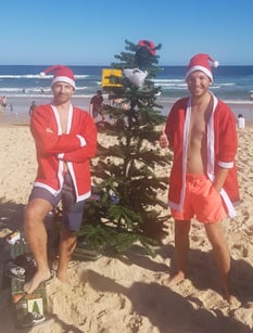 freaky finance, Hamsterrad Austeiger, Bondi Beach, Sydney, Heilig Abend, 2 Weihnachtsmänner am Strand und Tannenbaum