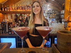 Blonde young female bartender with two red and white cocktails in Martini glasses in Distillers Republic bar in Old Riga