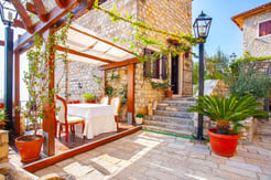 Charming outdoor dining terrace with covered pergola, white tablecloth, and stone steps leading to traditional Mediterranean stone Bey's house