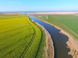 Luftaufnahme von einem flussähnlichen Gewässer zwischen zwei Feldern