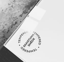 Uz rūdīta stikla redzams SKAISTUMA SMĒDE logotips ar marķējumu TEMPERED.