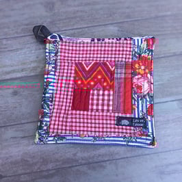 Manique en patchwork à dominante rouge et bouquets sur fond rayé bleu et blanc.