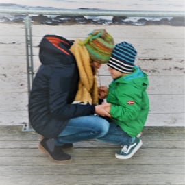 Imke mit ihrem Sohn Kopf an Kopf in der Hocke auf Steg am Meer