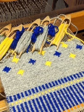 Deux grands coussins canapé à rayures exposés en plein air. Un coussin en rayures jaunes, oranges, marronnes, l'autre en rayures bleues, brunes et noires sur un fond de laine gris clair.