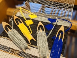 Deux grands coussins canapé à rayures exposés en plein air. Un coussin en rayures jaunes, oranges, marronnes, l'autre en rayures bleues, brunes et noires sur un fond de laine gris clair.