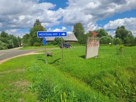 Sign pointing to the Soviet-era Mound of Friendship memorial in Latgale, Latvia, surrounded by grass and blue sky