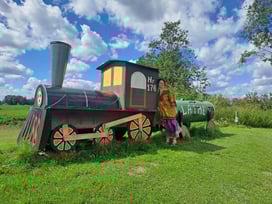 Large toy train advertissing the Museum of Happiness in Indra, Latvia, with a dark haired girl in a yellow blouse posing in front