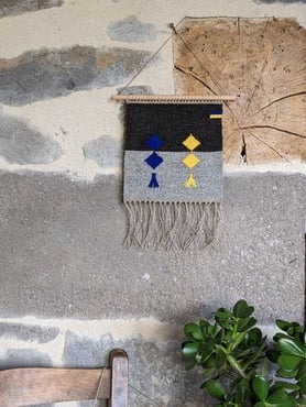 Deux grands coussins canapé à rayures exposés en plein air. Un coussin en rayures jaunes, oranges, marronnes, l'autre en rayures bleues, brunes et noires sur un fond de laine gris clair.