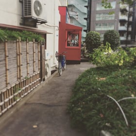 小道に入ると奥に赤い外壁の飲食店が見えます。お店の手前にビルの入口がございます。