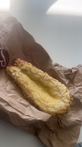 Bild einer Papiertüte auf dem Tisch, auf der eine Laugenstange, die mit Käse überbacken wurde, zusehen ist.