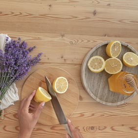 Citron coupé par un couteau en métal sur une planche en bois avec d'autres citrons coupés et du miel ainsi que des fleurs de lavande sur une table en bois