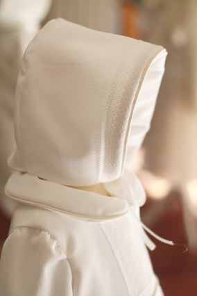 Bonnet baptême hiver bébé garçon en velours de coton blanc cassé et dentelle de Calais avec une doublure polaire. Création française Fil de Légende. Magasin vêtements baptême Paris, Neuilly-sur-Seine. Expéditions en France et à l'international.