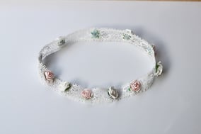 Bandeau cheveux cérémonie bébé en dentelle élastique avec des fleurs blanches et roses. Création française Fil de Légende. Magasin vêtements baptême Paris, Neuilly-sur-Seine. Expédition en France et à l'international.