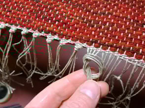 La finition d'un tapis tissé - la frange en fils de lin est nouée.