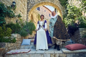 Cervantes & Dulcinea walking through a historic stone archway at Palata Venezia, surrounded by greenery and Mediterranean charm