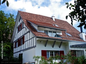 Fitze Dach AG Steildach mit Lukarne an einem schönen Riegelhaus, mit Biberschwanzziegeln bedeckt.