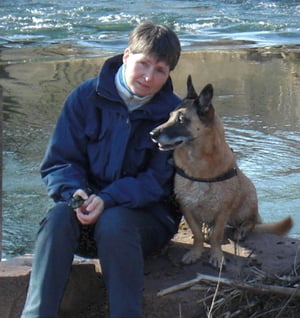 Frau sitzt mit Hund am Fluss.