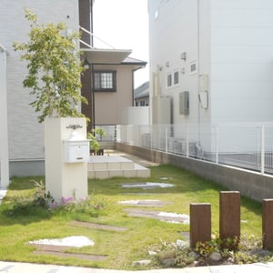 緑のじゅうたんの中に、コンクリート製の枕木と化粧砂利を疎らに配することで、軽やかな印象のアプローチになりました。合間合間に、芝生のふかふかした感触も味わいながらゆっくり味わって欲しいところです。門柱も、敢えてシンプルな角柱にすることで表札,ポストと共に外壁に溶け込んでいます。　　　　　　　　　　　　　　　　　　　　　　　　　　　　　　　　　　　　　　　　　　　　　　　倉敷市　T様邸　フラワーチルドレン　エクステリア