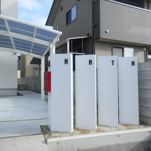 用水沿いの擁壁に対して斜め30度に振った門塀を分離して立て、それぞれに表札を分けてつけました。書体もデザインコンセプトに合ったものを慎重に選びました。エクステリアでよく使う塗料はあえて使わず、ポリウレタン樹脂塗装を採用し、門塀の質感にもこだわりました。　　　　　　　　　　　　　　　　　　　　　　　　　　　　　　　　　　　　　　　　　　　　　　　　　　　　　　　　　　　倉敷市中島　Ｈ様邸　エクステリア　フラワーチルドレン