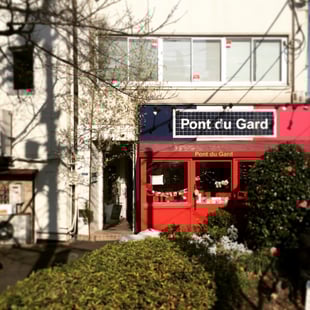 橋を渡りきった所で右を見て頂くと赤い外壁の飲食店が見えます。お店の左側がビルの入口になります。