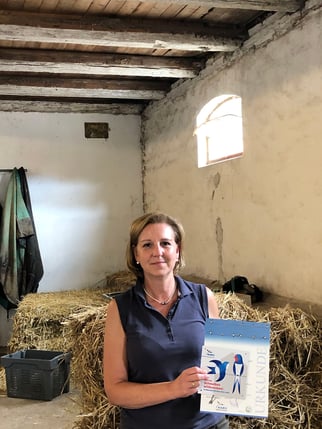 Frau Henkels hält lächelnd Plakette und Urkunde in die Kamera