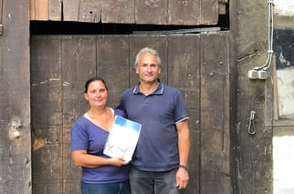 Familie Grube steht vor einem Holztor und hält lächelnd Plakette und Urkunde in die Kamera