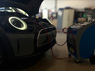 alt="Klimaservice wird mit einem grau-orangenen Klimagerät an einem dunklen BMW durchgeführt."