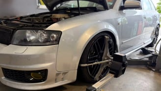 alt="graues Fahrzeug in der Werkstatt, während eine Achsvermessung durchgeführt wird."