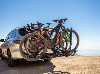 alt="Silbernes Auto mit montierten Fahrradträger am Heck, beladen mit Fahrrädern, blauer Himmel im Hintergrund."