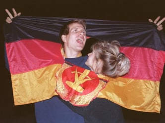 Der Tag der Wiedervereinigung vor 25 Jahren: Ein jubelndes Paar hat sich in einer DDR-Fahne dort Platz geschaffen, wo vorher das Emblem mit Hammer und Sichel. Foto: Archiv