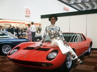 Eine junge Frau posiert auf der Internationalen Automobil-Ausstellung in Frankfurt am Main 1969 auf einem roten Lamborghini Miura S. Der Sportwagen verfügt über einen Hubraum von 3929 ccm, 370 PS und eine Spitzengeschwindigkeit von 300 km/h. Foto: Gutberl