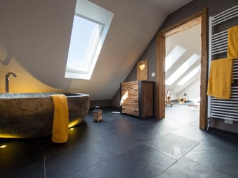 Reizvoller Kontrast: Leuchtendes Gelb, antikes Holz und ein charaktervoller Natursteinboden vervollständigen das Badezimmer (Foto: jonastone GmbH und Co. KG)