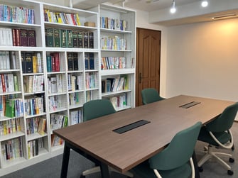写真：打ち合わせスペース。4人がけテーブルの後ろに大きな本棚がある。