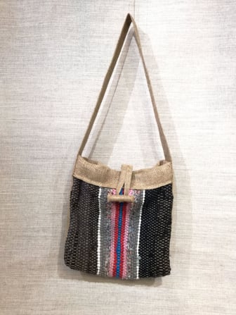 Grand sac à bandoulière, tissé en lirette à rayures brun, gris rouge et rose. Les finitions sont en jute.