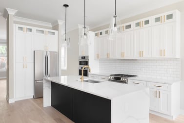 A luxury white kitchen with black pendant lights hanging above a waterfall granite island, stainless steel Bosch appliances, and gold hardware