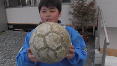 宝物のサッカーボールを手に、インタビューに答える少年、この時のインタビューをもとに 「帰ってきたサッカーボール」を創作。