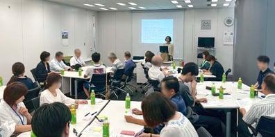 大勢の社員が聴講する会議室で研修を行う菅野昭子