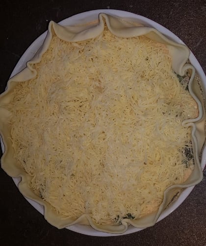 geriebener Käse auf einer Mürbeteig Quiche mit Mangold Füllung