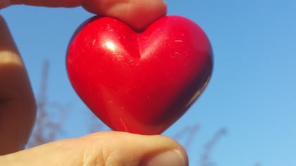 Rotes Steinherz wird gegen den blauen Himmel gehalten